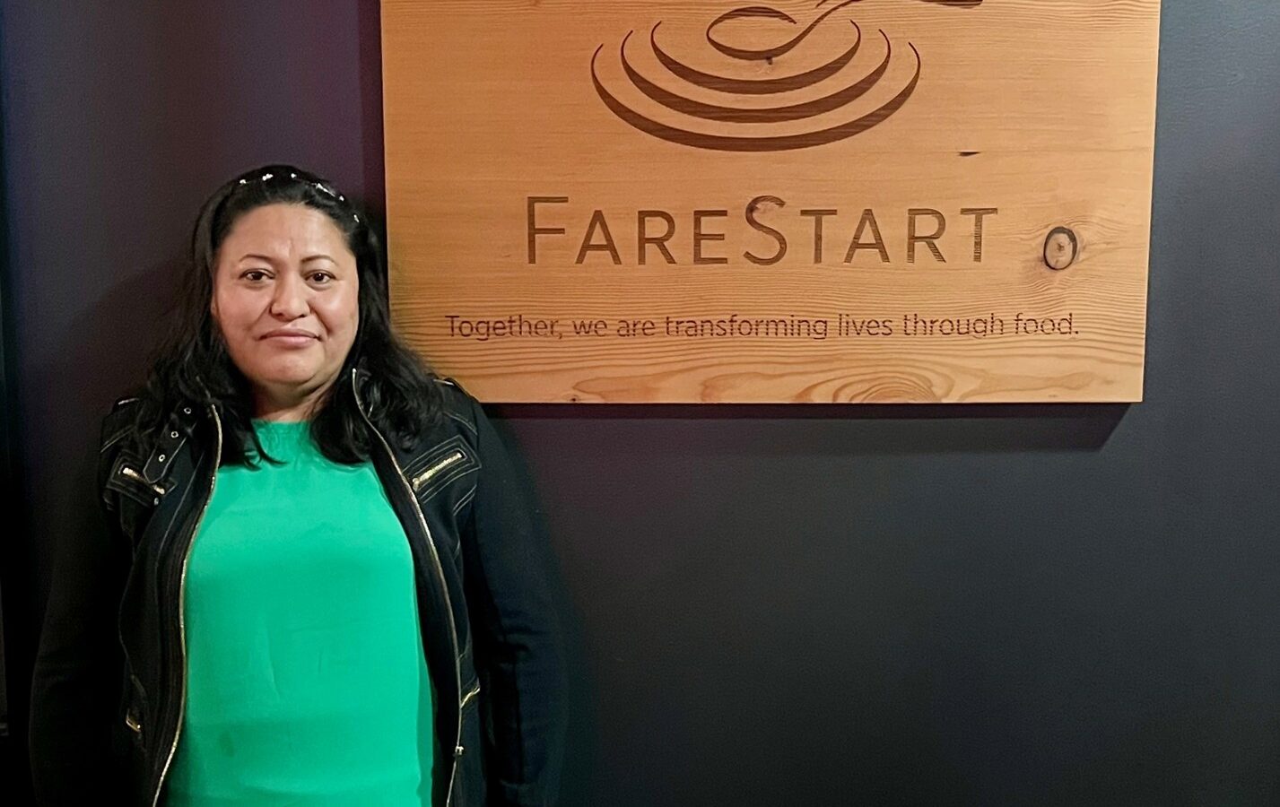 Adriana, a FareStart graduate, posing with the FareStart sign in the FareStart Restaurant